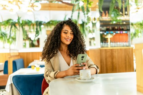 Smiling woman using date app sitting on a cafeteria